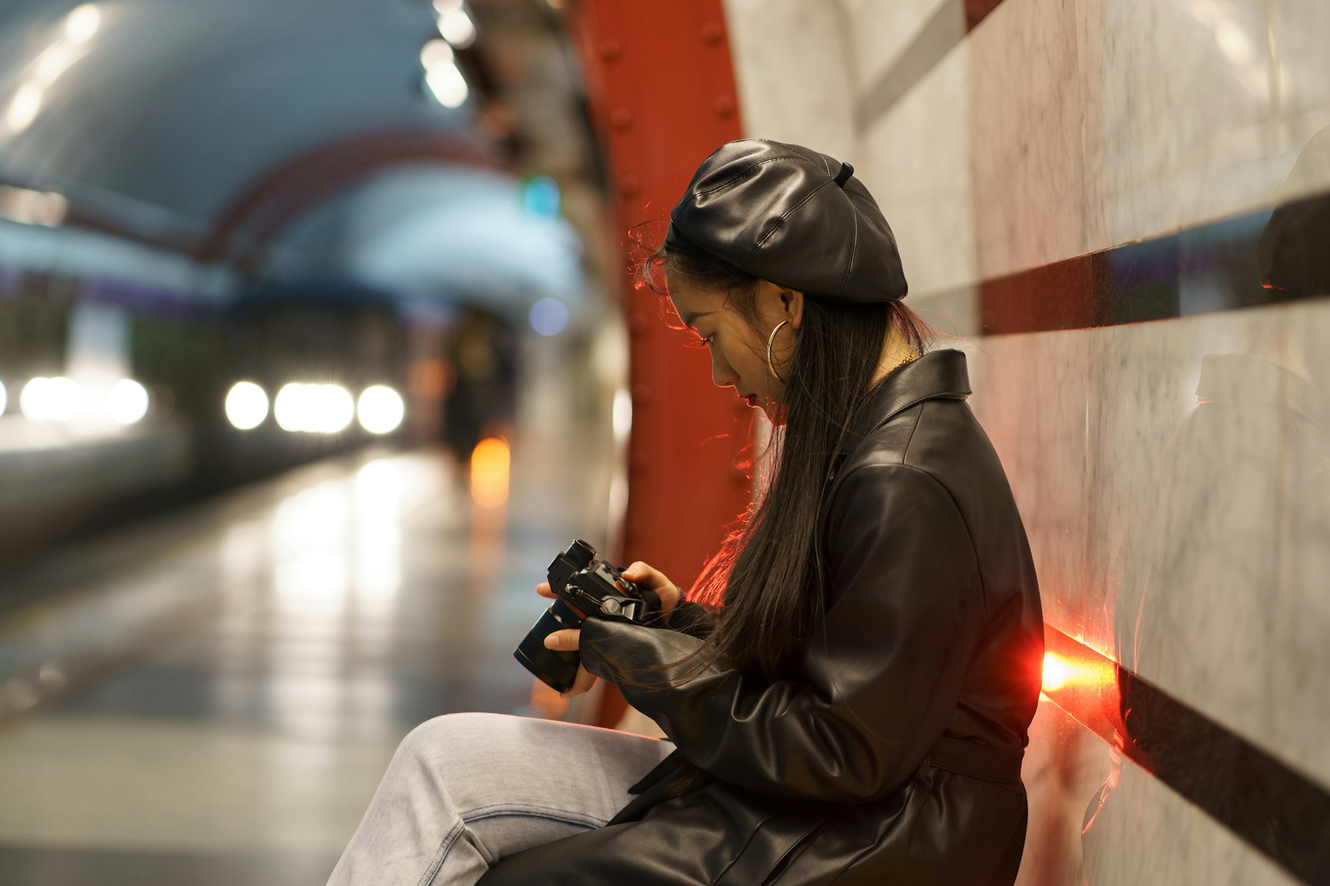 Young woman looks at photos on camera while waiting in metro station for train